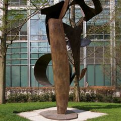 A brown sculpture in an outdoor space. The sculpture is made up of different shaped pieces.